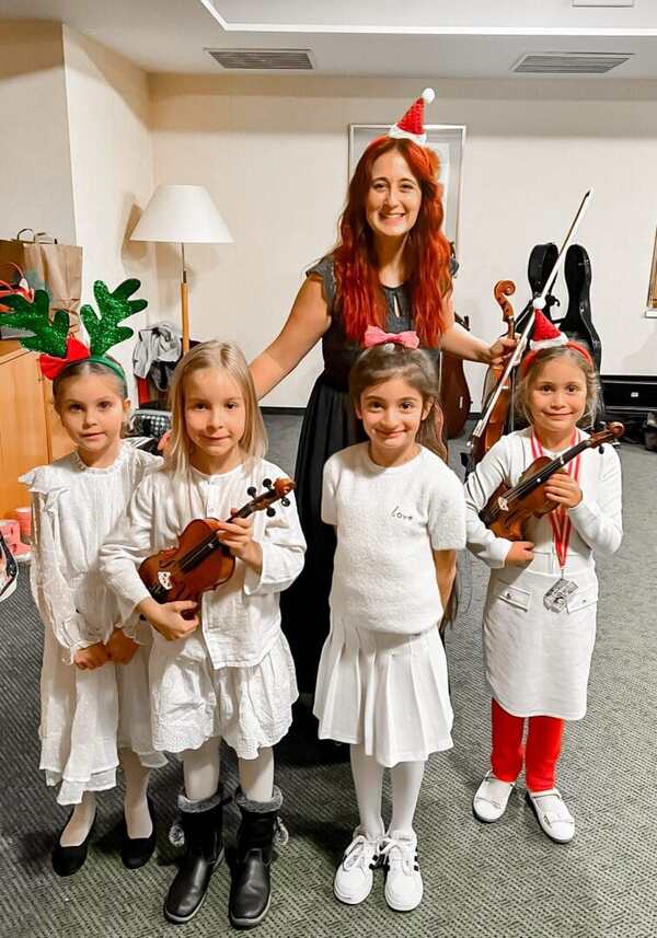 Children playing violins at El Sistema Austria holiday celebration with festive accessories, joyful music performance.